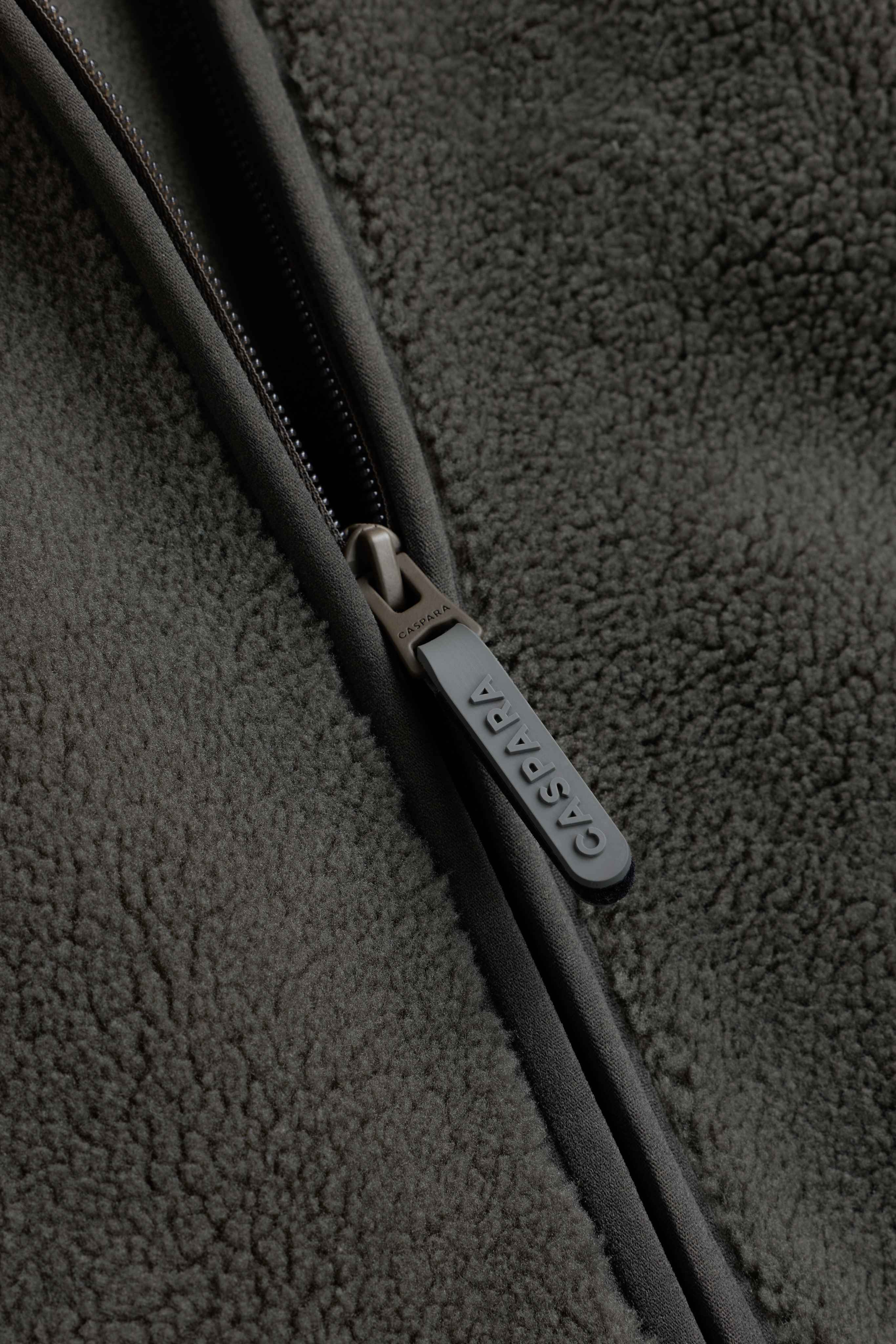 Close-up of the branded CASPARA zipper pull on a textured khaki fleece vest.
